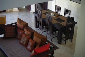 Un comedor con una mesa rectangular y seis sillas, un sofá con cojines estampados y un suelo de baldosas.