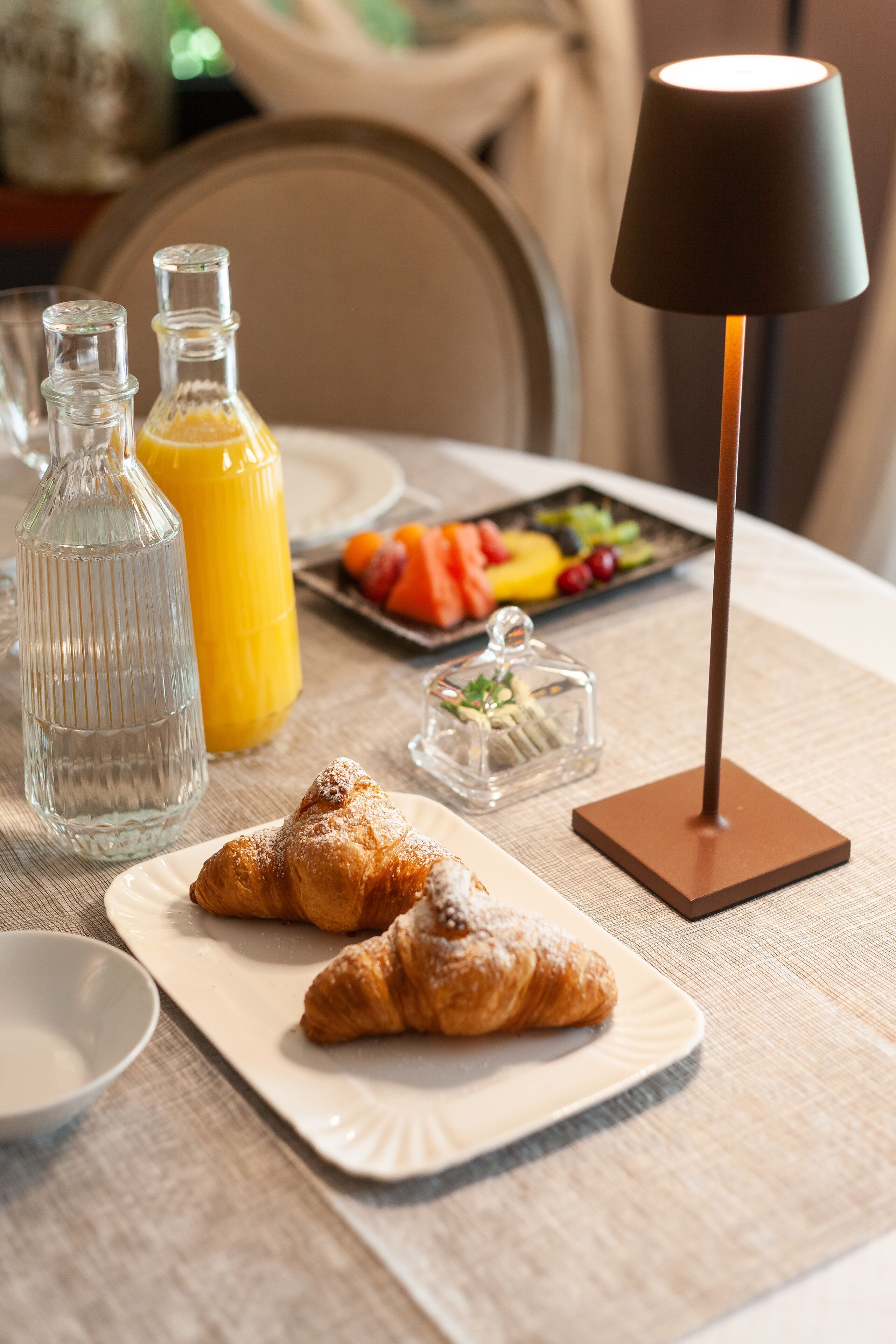 A breakfast setting with croissants, juice, and a fruit platter on a table.
