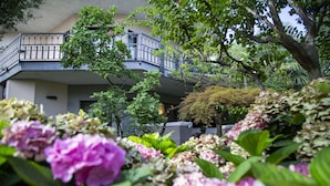 A building with a balcony, surrounded by lush greenery and flowering plants. - Like Home - Boutique Hotel (Azzano San Paolo)