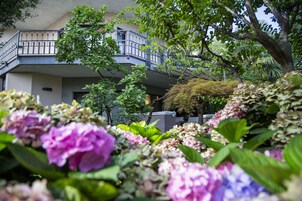 Un edificio con un balcone, circondato da vegetazione lussureggiante e piante fiorite.