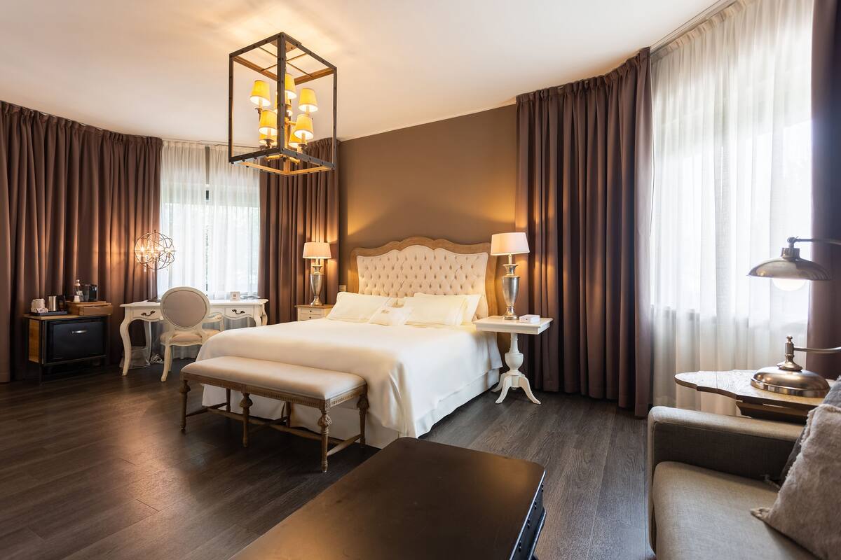 Una habitación de hotel con una cama grande, un escritorio, una silla, un banco y una mesa.