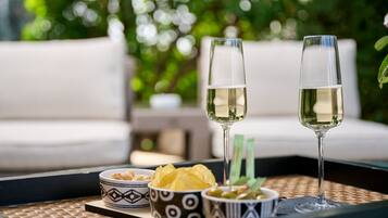 A tray with two glasses of white wine, a bowl of chips, and a bowl of olives on a woven mat.