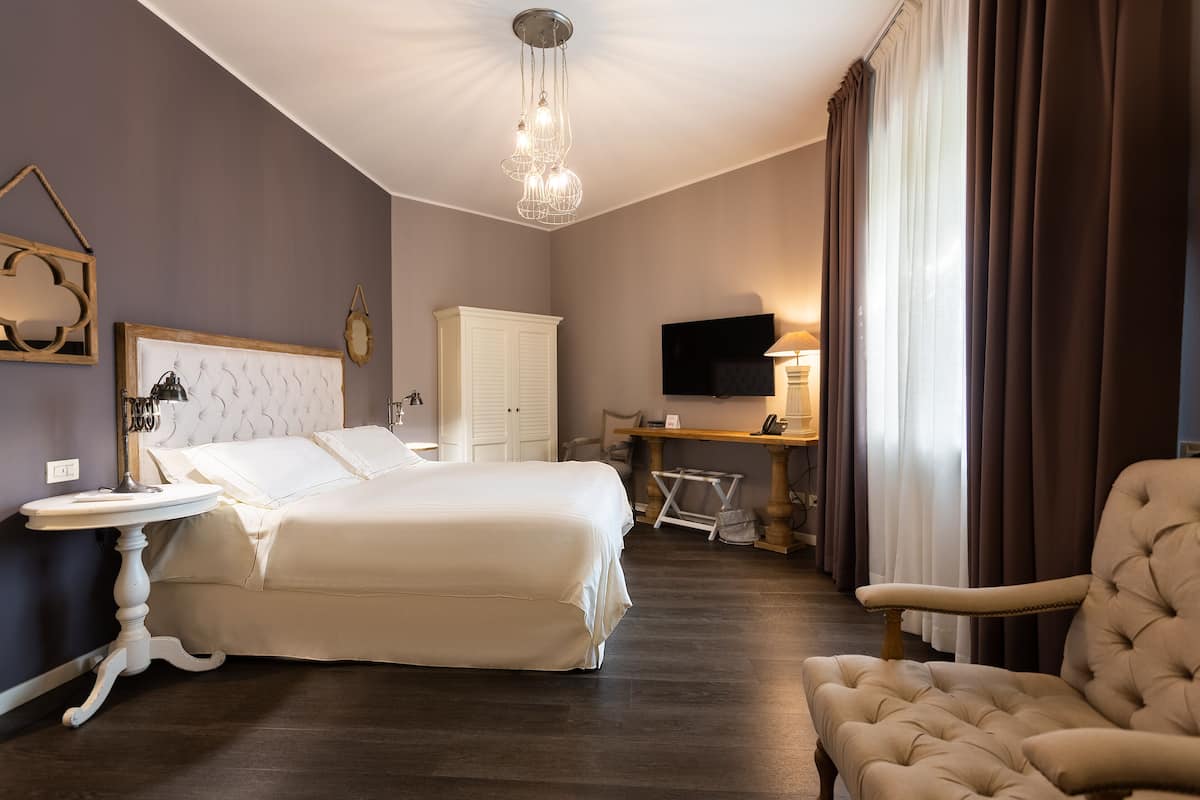 Una habitación de hotel con una cama grande, un escritorio, una silla, un televisor y una araña.