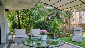 A covered outdoor seating area with a glass table, wicker chairs, and a potted plant. - Like Home - Boutique Hotel (Azzano San Paolo)