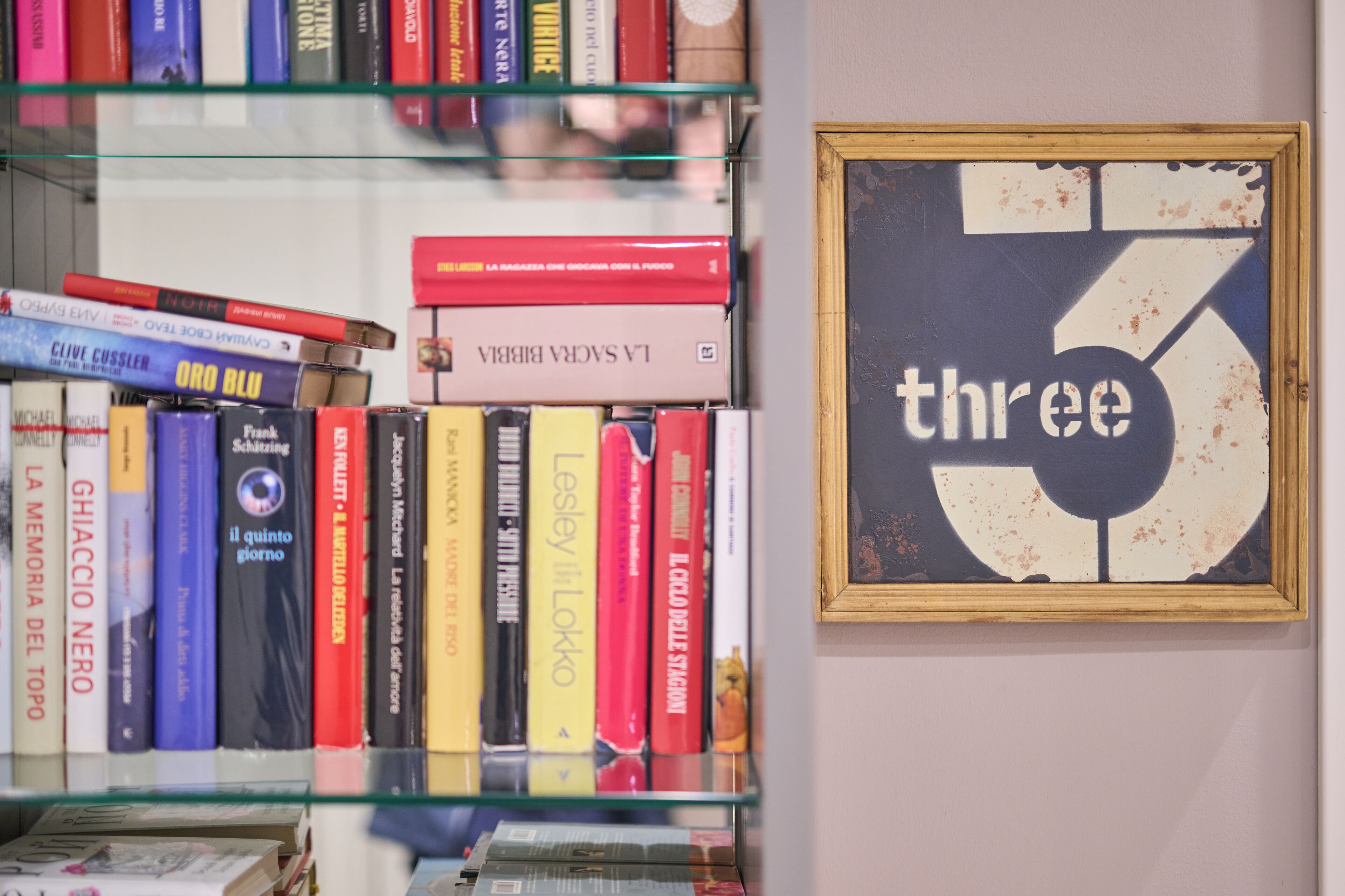 Une bibliothèque remplie de divers livres et un panneau encadré sur lequel on peut lire le mot « trois ».