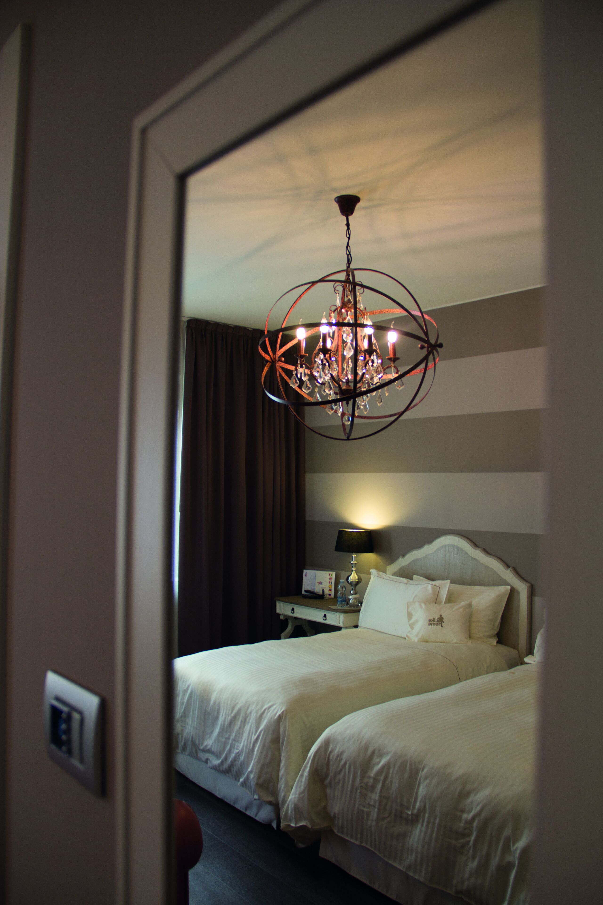 A hotel room with a large bed, a bedside table with a lamp, and a chandelier.