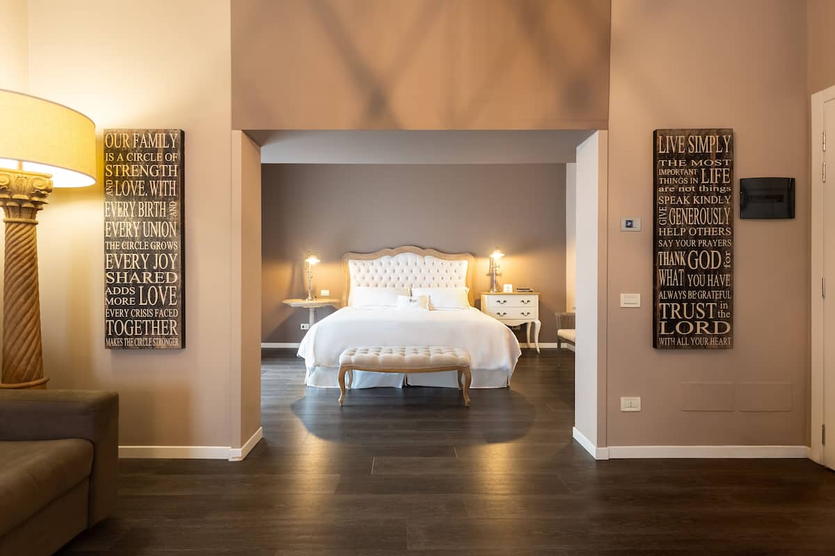Un dormitorio con una cama grande, mesitas de noche, un banco y decoración inspiradora en la pared.