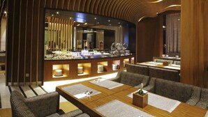Een moderne hotellobby met een gebogen houten plafond, een centraal gelegen bar en zitgedeeltes met tafels en stoelen.