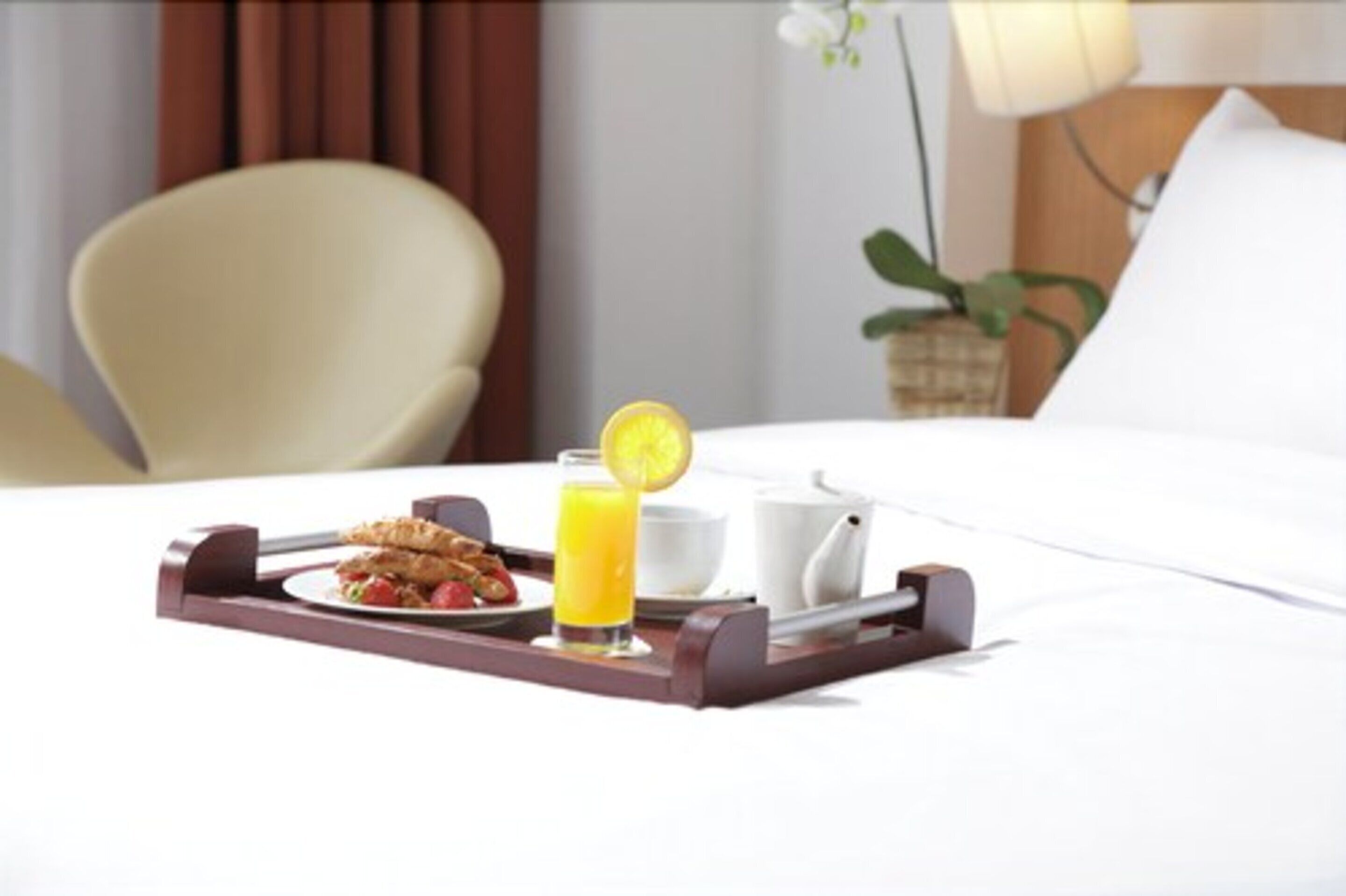 Bandeja de desayuno con cruasanes, un vaso de jugo de naranja y una taza blanca sobre la cama.