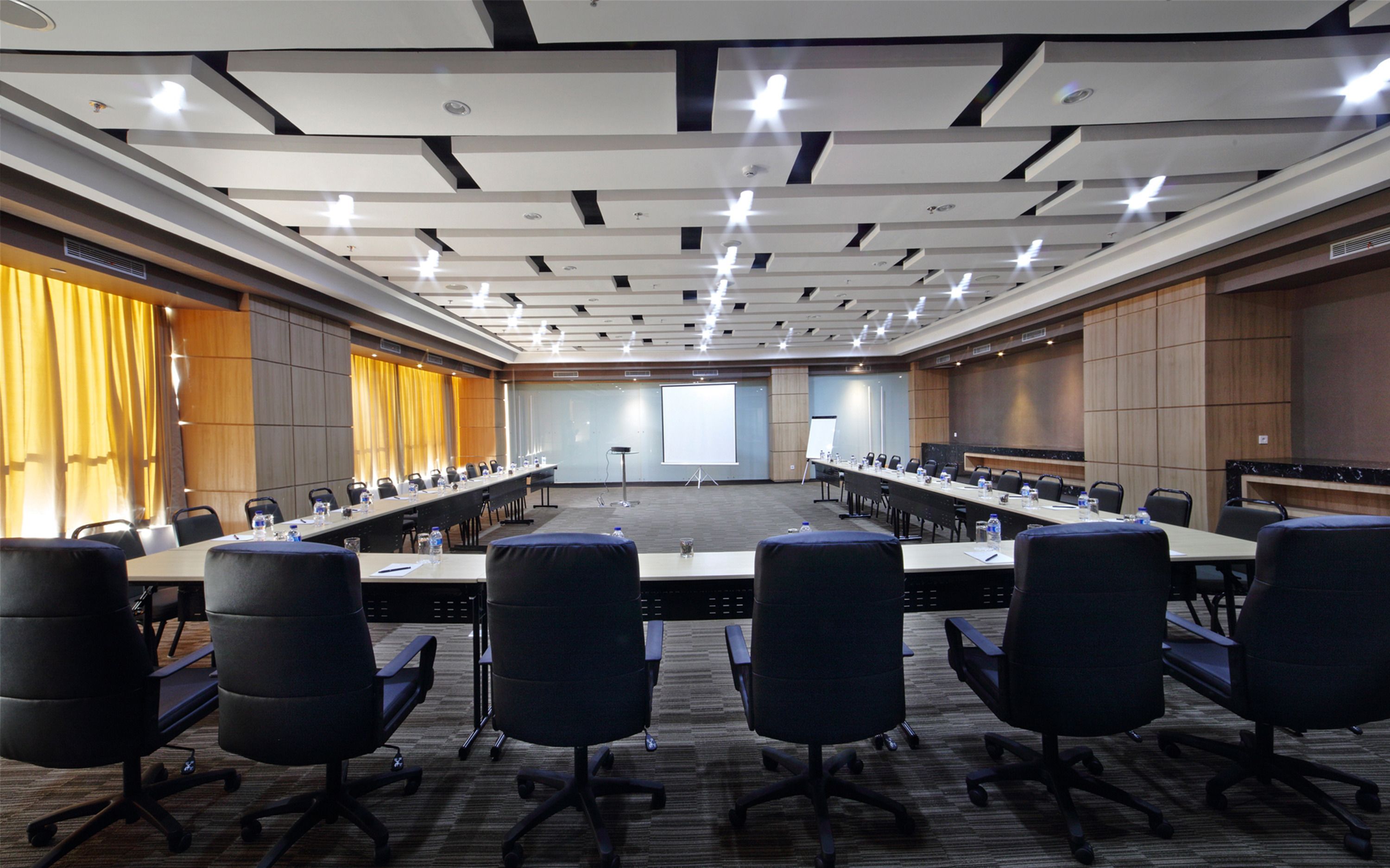 A conference room with a long table, multiple chairs, a projector screen, and a whiteboard.