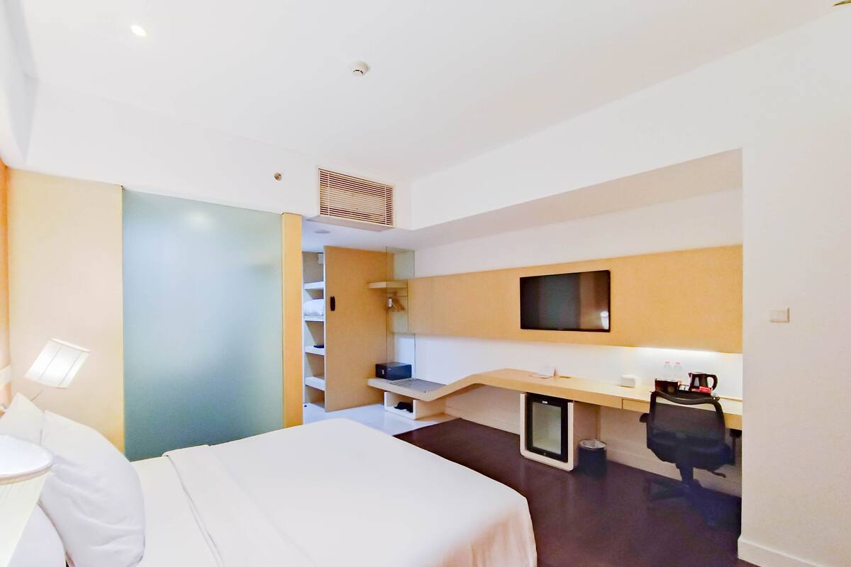 Une chambre d’hôtel moderne équipée d’un lit, d’un bureau, d’une chaise, d’une télévision et d’une petite kitchenette.