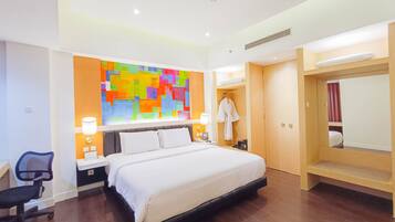 Habitación de hotel con una cama grande, mesitas de noche, un escritorio, una silla, un cuadro abstracto colorido, una bata y un armario.