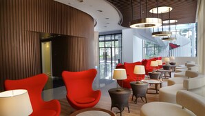Een moderne lobby met rode en beige zitplaatsen, een glazen wand en een plafond met ronde lampen.