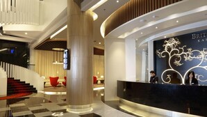 Een moderne hotellobby met een receptiebalie, een trap en een zithoek.