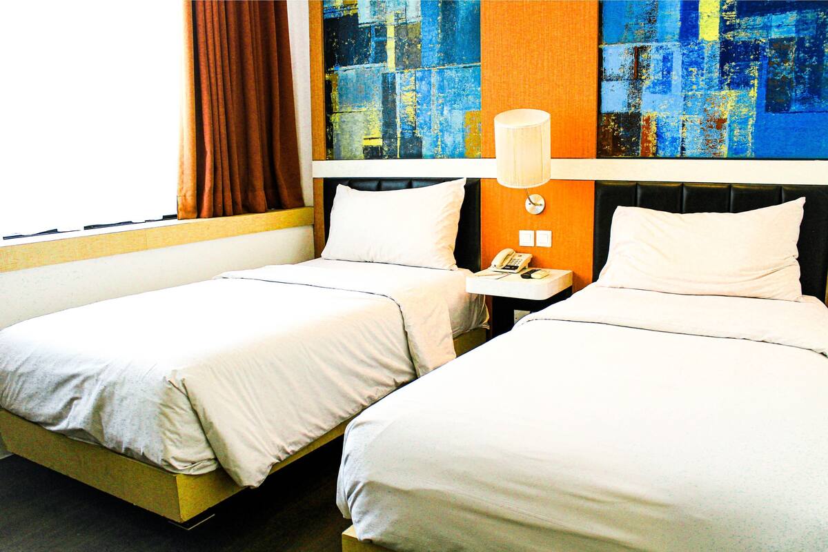 Une chambre d’hôtel avec deux lits, une table de chevet avec un téléphone et une grande peinture abstraite au mur.