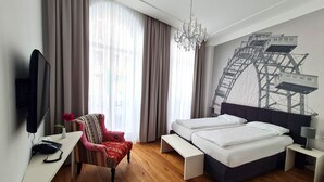 Een hotelkamer met een bed, een bureau met telefoon, een stoel, een televisie en een groot raam met gordijnen.