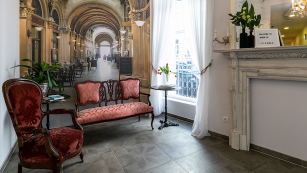 Een hotellobby met een rode bekleden bank, een klein rond tafeltje met een bloevas, en een open haard met een bord boven.'