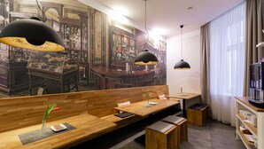 Een modern restaurant met houten banken en tafels, hanglampen en een muurschildering van een barscène.