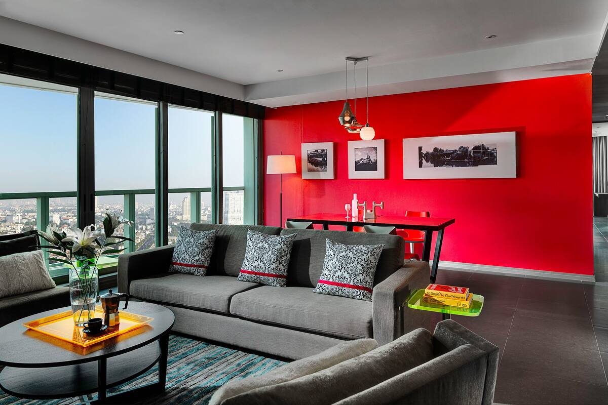 Un salon moderne avec un mur d’accent rouge, un canapé gris et une table basse agrémentée d’un vase et d’une théière.