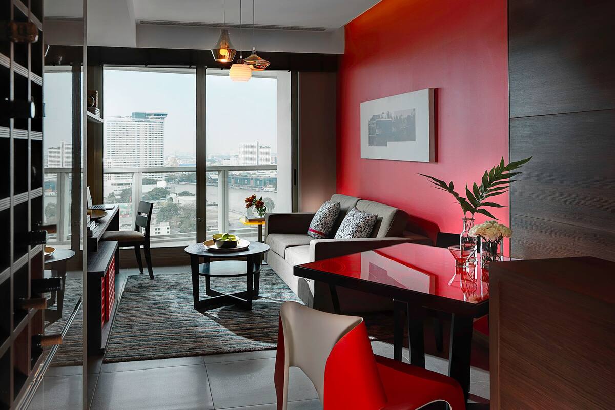 Un salon moderne avec vue sur la ville, un mur d’accent rouge et un coin repas avec une table en verre.