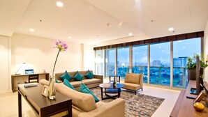 A modern living room with a sofa, coffee table, and a view of the city through large windows. - Klapsons The River Residences Bangkok (Bangkok)