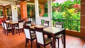 Un restaurante con terraza, mesas y sillas de madera, rodeado de exuberante vegetación.