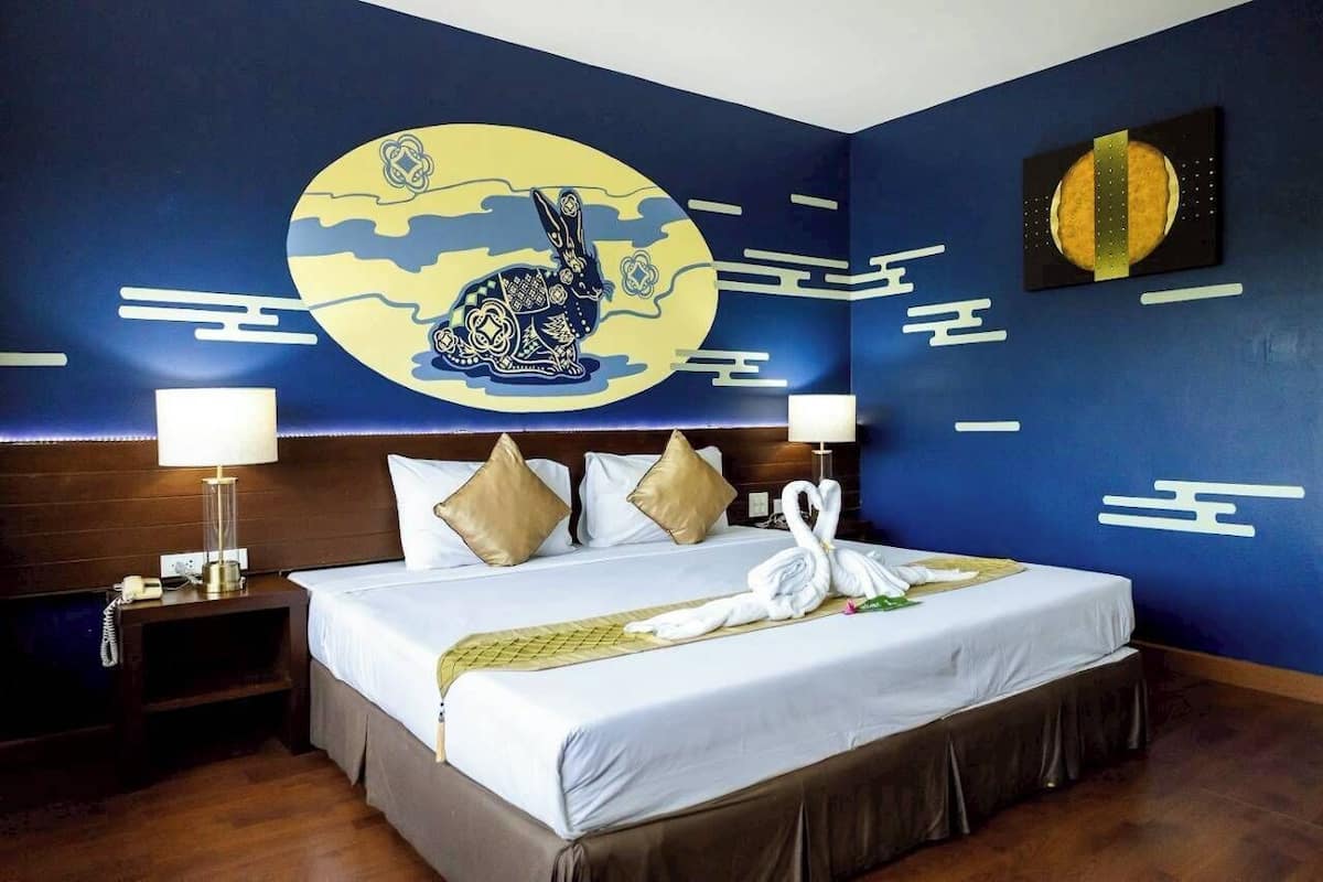 A hotel room with a large bed, two bedside tables, a wall with a circular artwork, and a bedspread with a swan design.