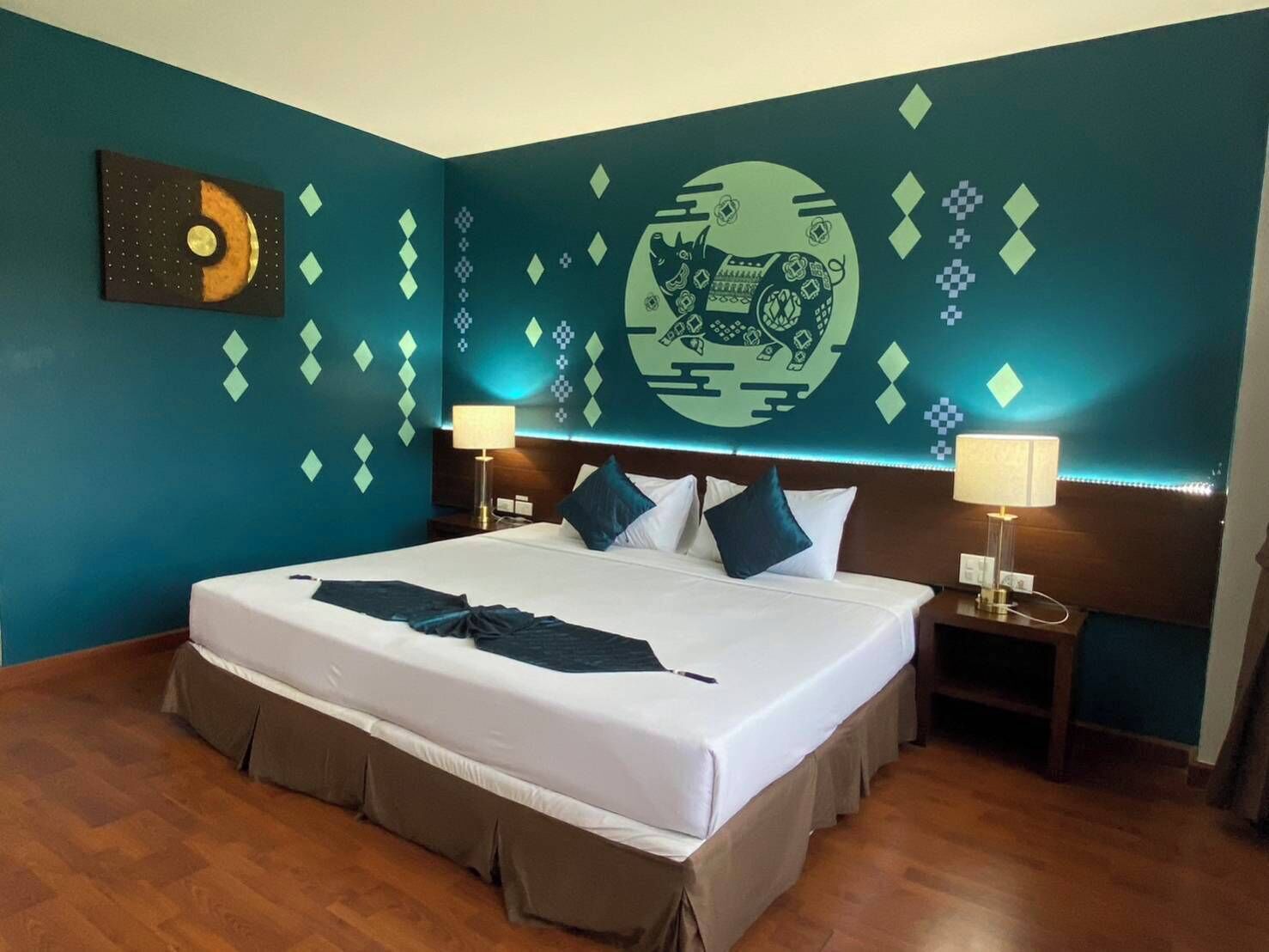A hotel room with a large bed, two bedside tables, a wall mural, and a wooden floor.