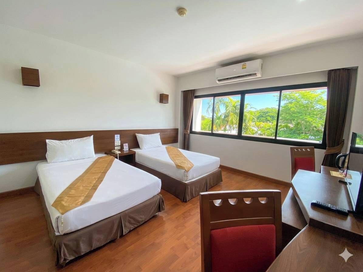 Une chambre d’hôtel avec deux lits, un bureau, une chaise et une grande fenêtre donnant sur un paysage verdoyant.