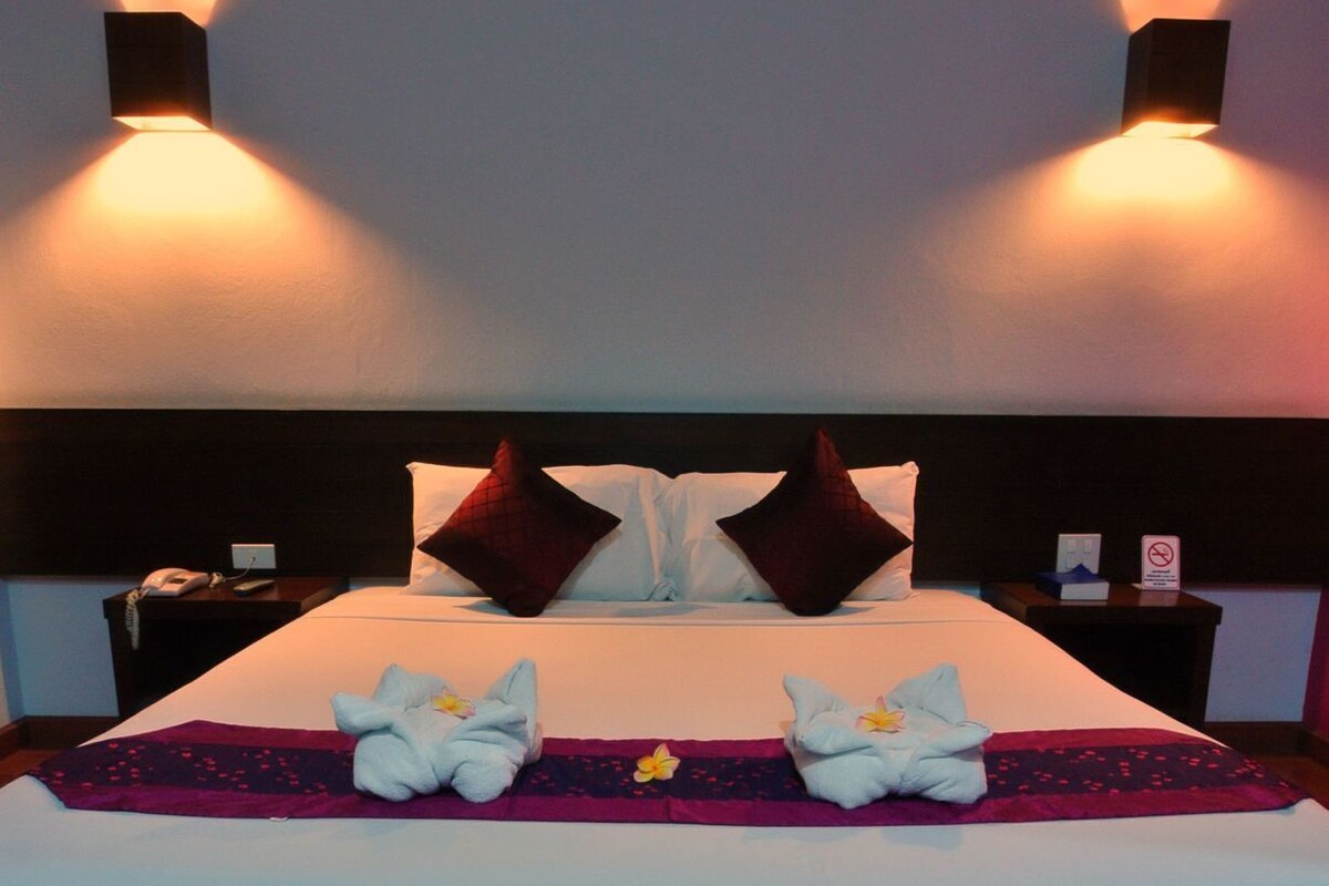 A hotel room with a bed, pillows, a nightstand, a phone, and wall-mounted lights.