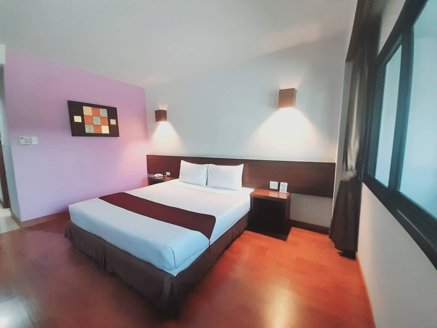 Ein Hotelzimmer mit einem großen Bett, einem Nachttisch, einer Wandleuchte und einem Fenster.
