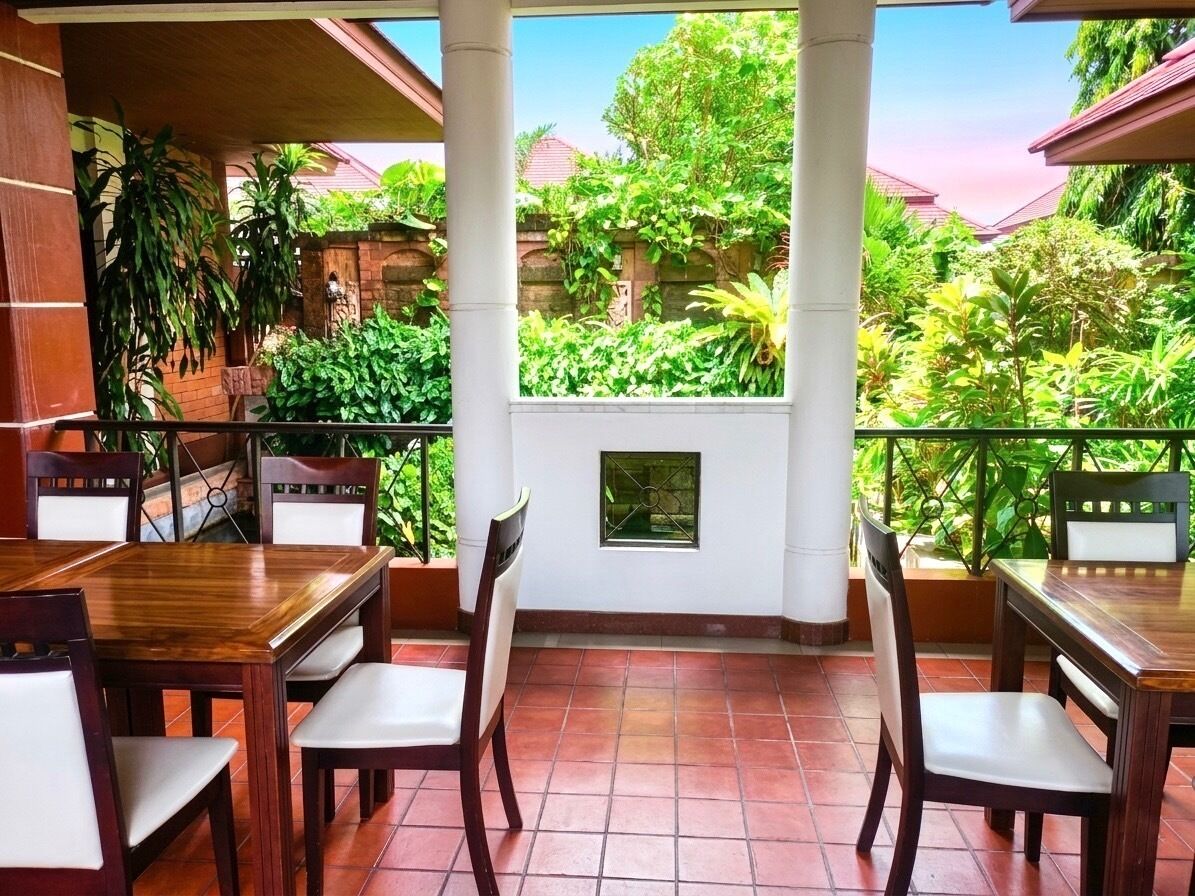A covered outdoor dining area with a view of lush greenery and a stone wall.