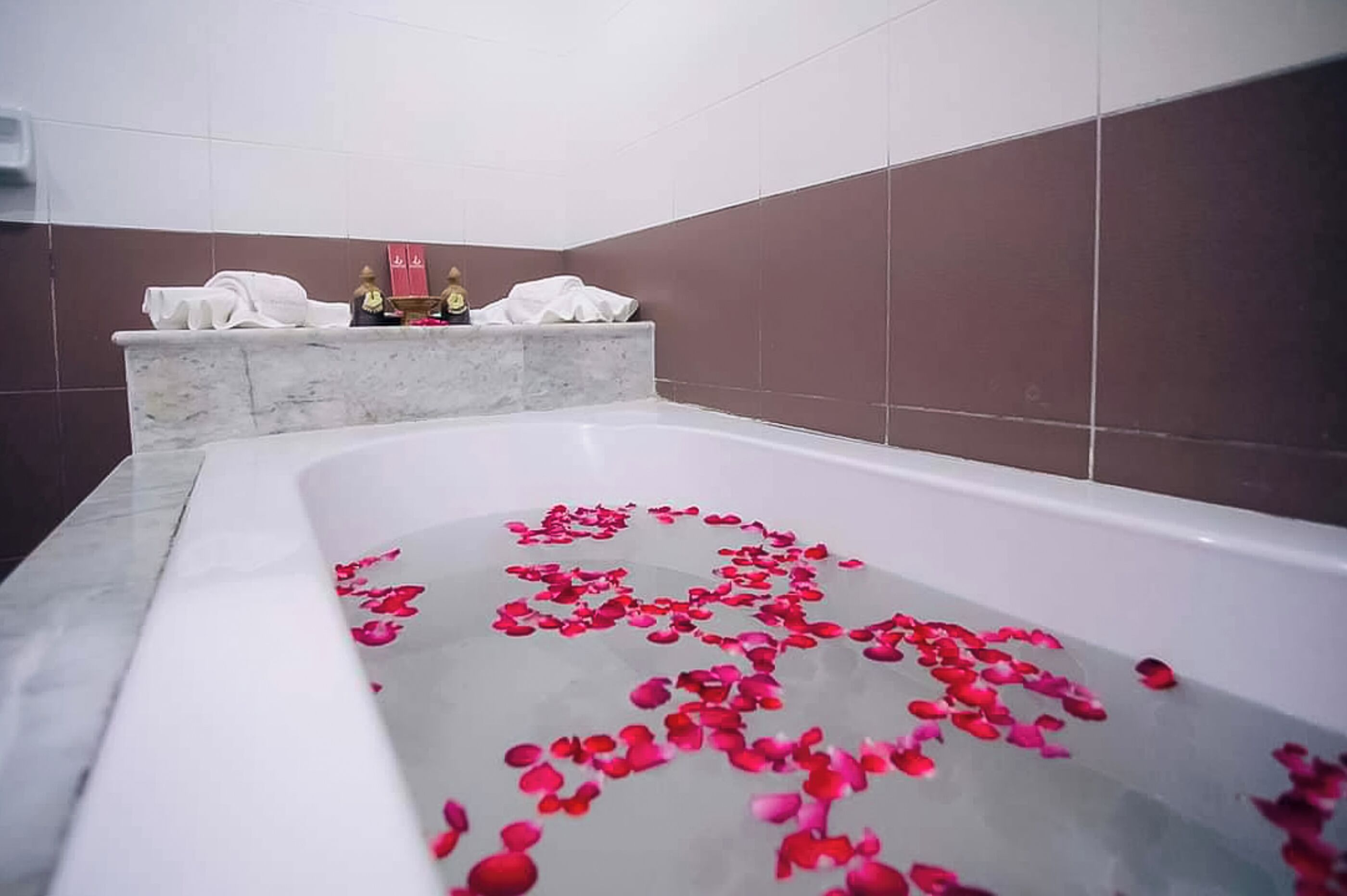 A bathtub filled with rose petals, marble steps, and a towel rack with towels.