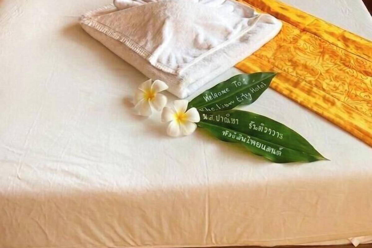 A neatly made bed with a white pillow, a folded towel, and a yellow decorative strip.