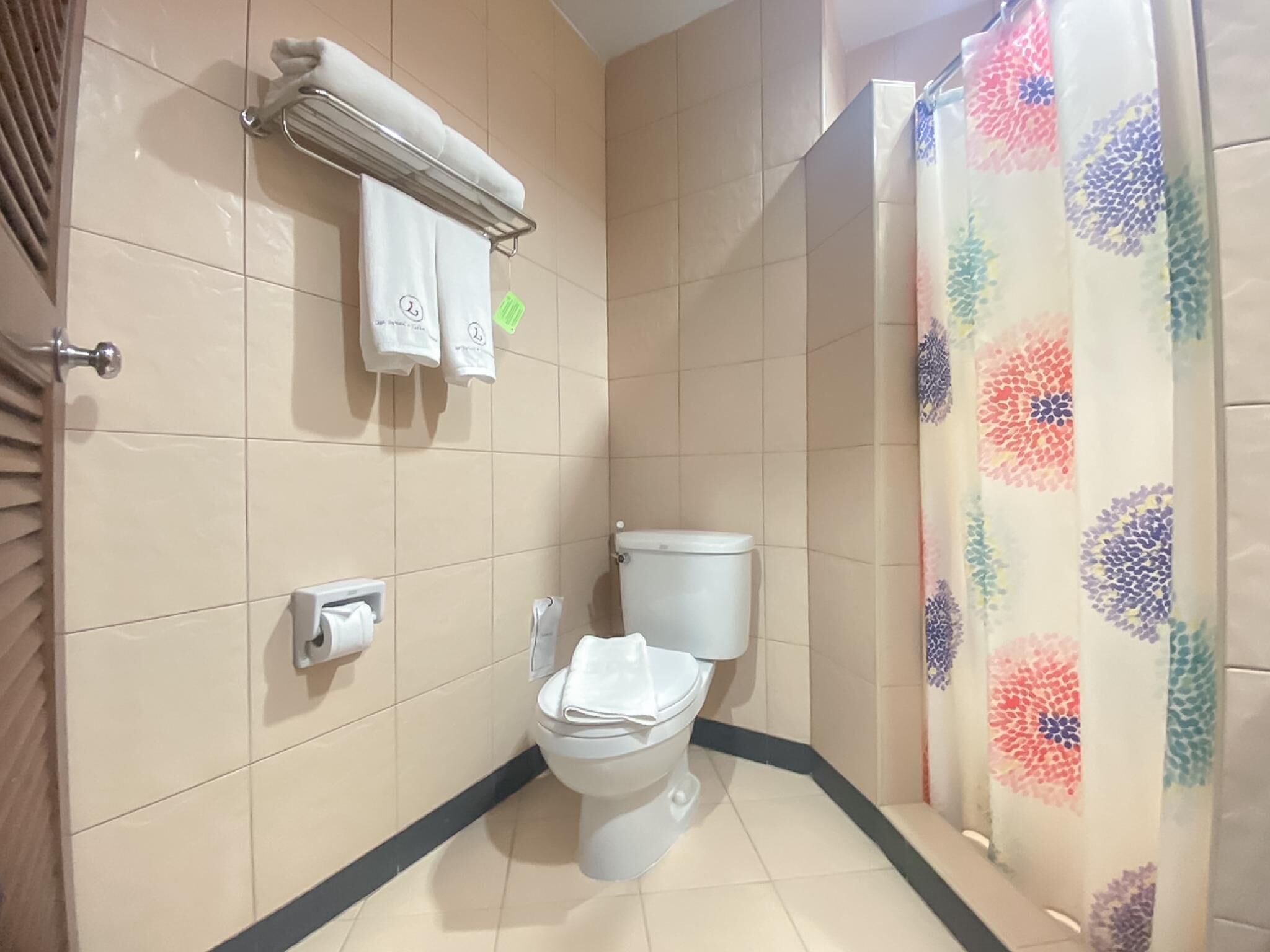 A bathroom with a toilet, a towel rack with two towels, a toilet paper holder, and a shower curtain with a floral pattern.