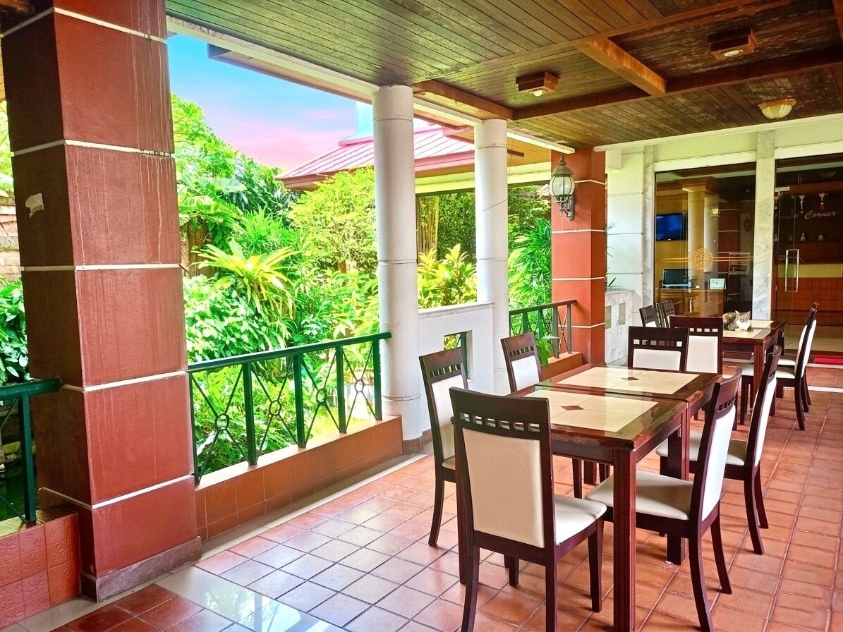 Un área de comedor al aire libre techada con terraza, sillas de madera y vistas a exuberante vegetación.