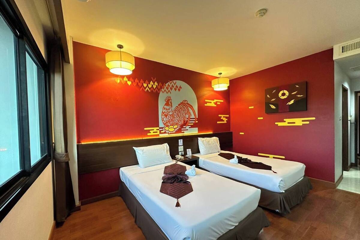 A hotel room with two beds, a large window, and a red accent wall with artwork.
