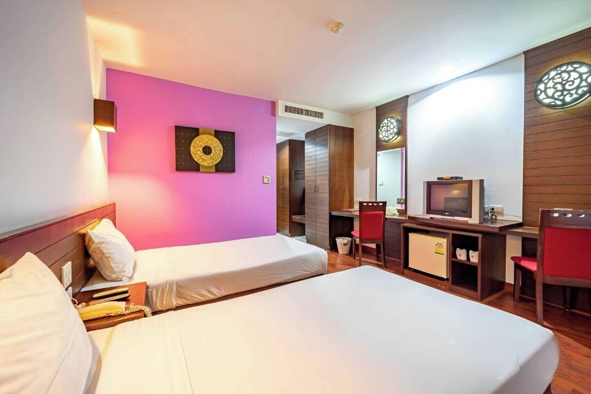 A hotel room with two beds, a desk with a television, a mirror, and a decorative wall piece.