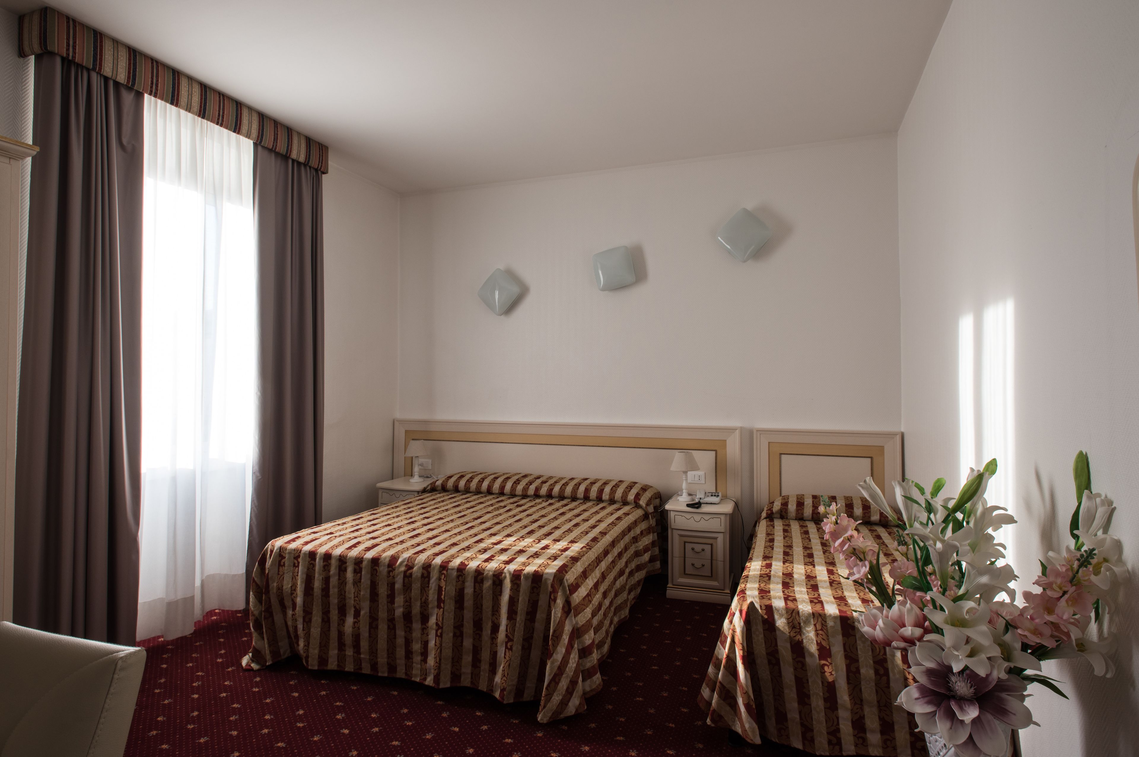 Une chambre d’hôtel avec deux lits, une table de chevet, une chaise et un vase de fleurs.