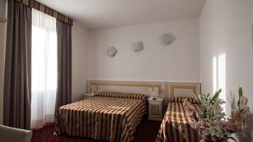 Une chambre d’hôtel avec deux lits, une table de chevet, une chaise et un vase de fleurs.