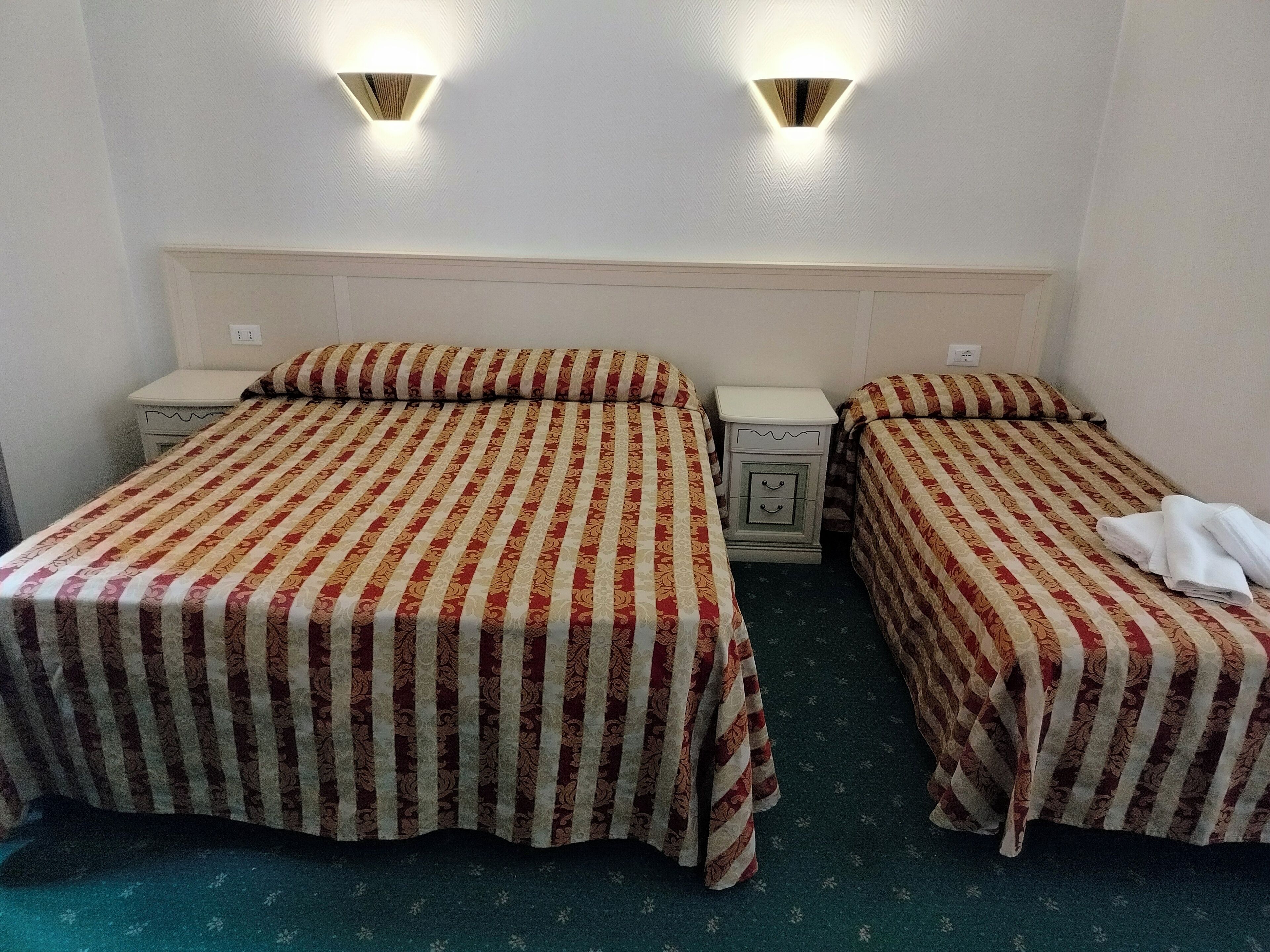 A hotel room with two beds, each with striped bedding, a nightstand, and a wall-mounted light fixture.