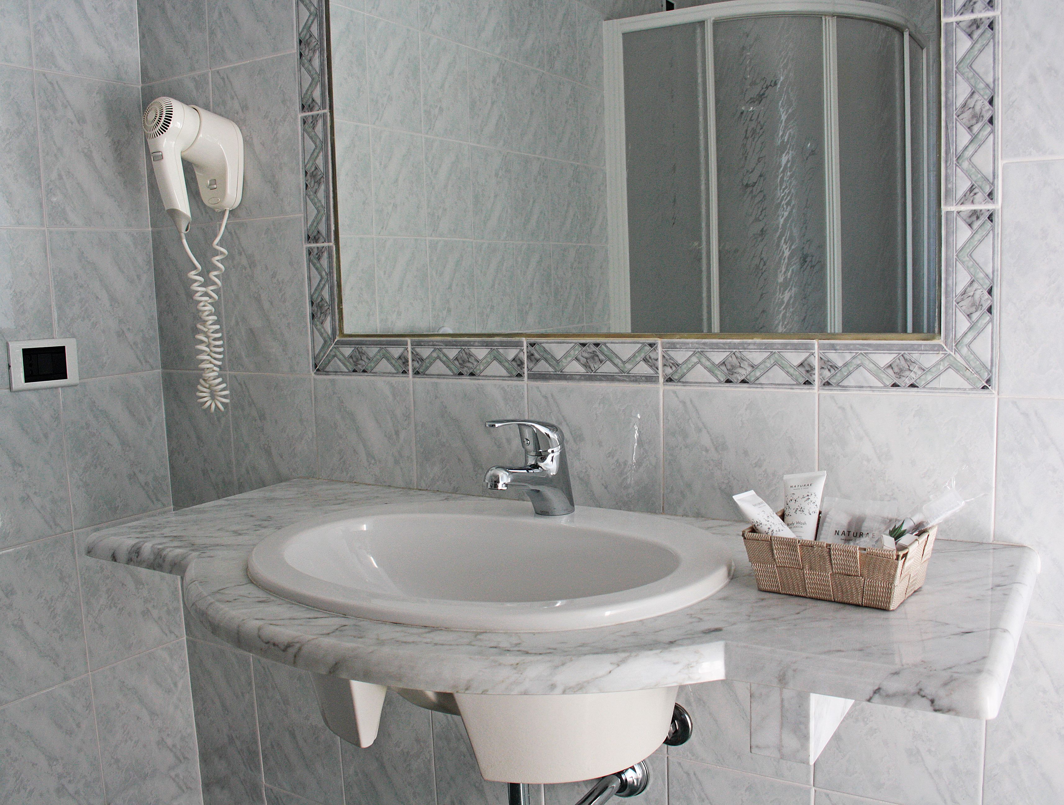 A bathroom with a marble sink, a hairdryer mounted on the wall, a mirror with a decorative frame, and a wicker basket on the countertop.