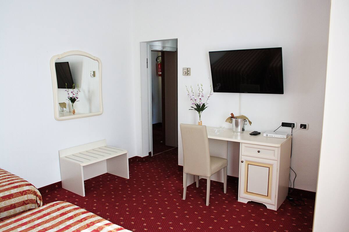 A hotel room with a bed, a desk with a chair, a TV, and a small cabinet.