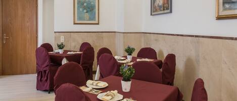A conference room with round tables, red chairs, and white tablecloths.