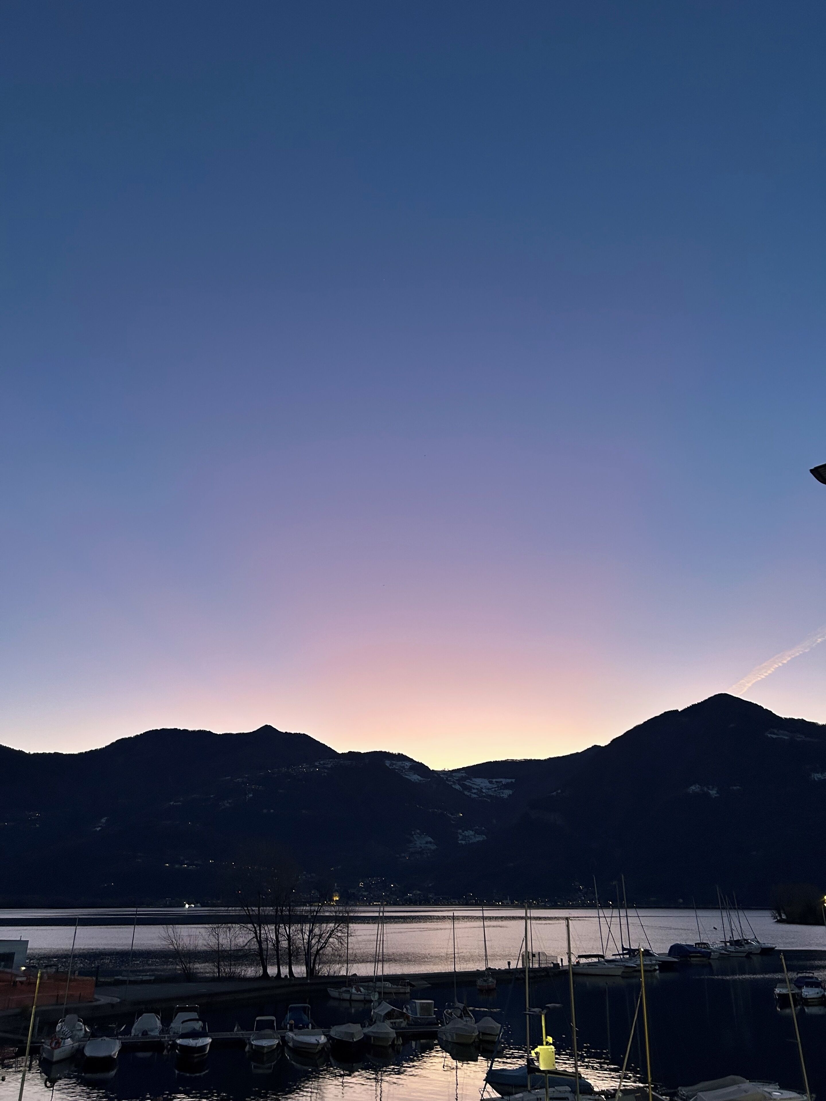 Un port de plaisance avec des bateaux amarrés, un lac paisible et des montagnes en arrière-plan.