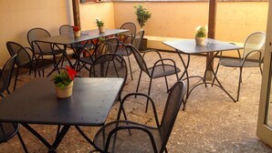 An outdoor patio with tables and chairs, potted plants, and a view of a bridge and mountains. - Ostello del Porto (Lovere)