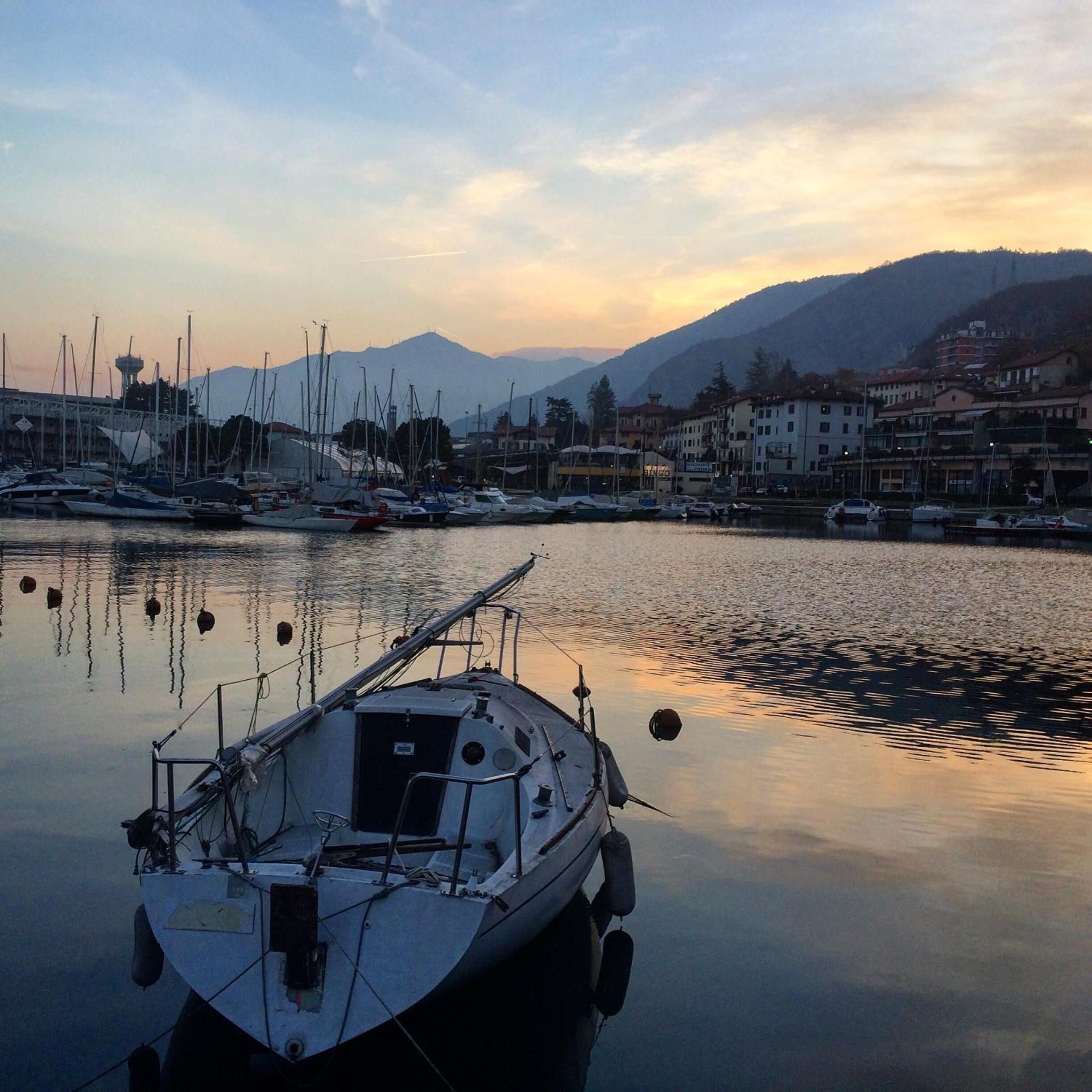 Un port de plaisance avec des bateaux amarrés, une eau calme et des bâtiments en arrière-plan.