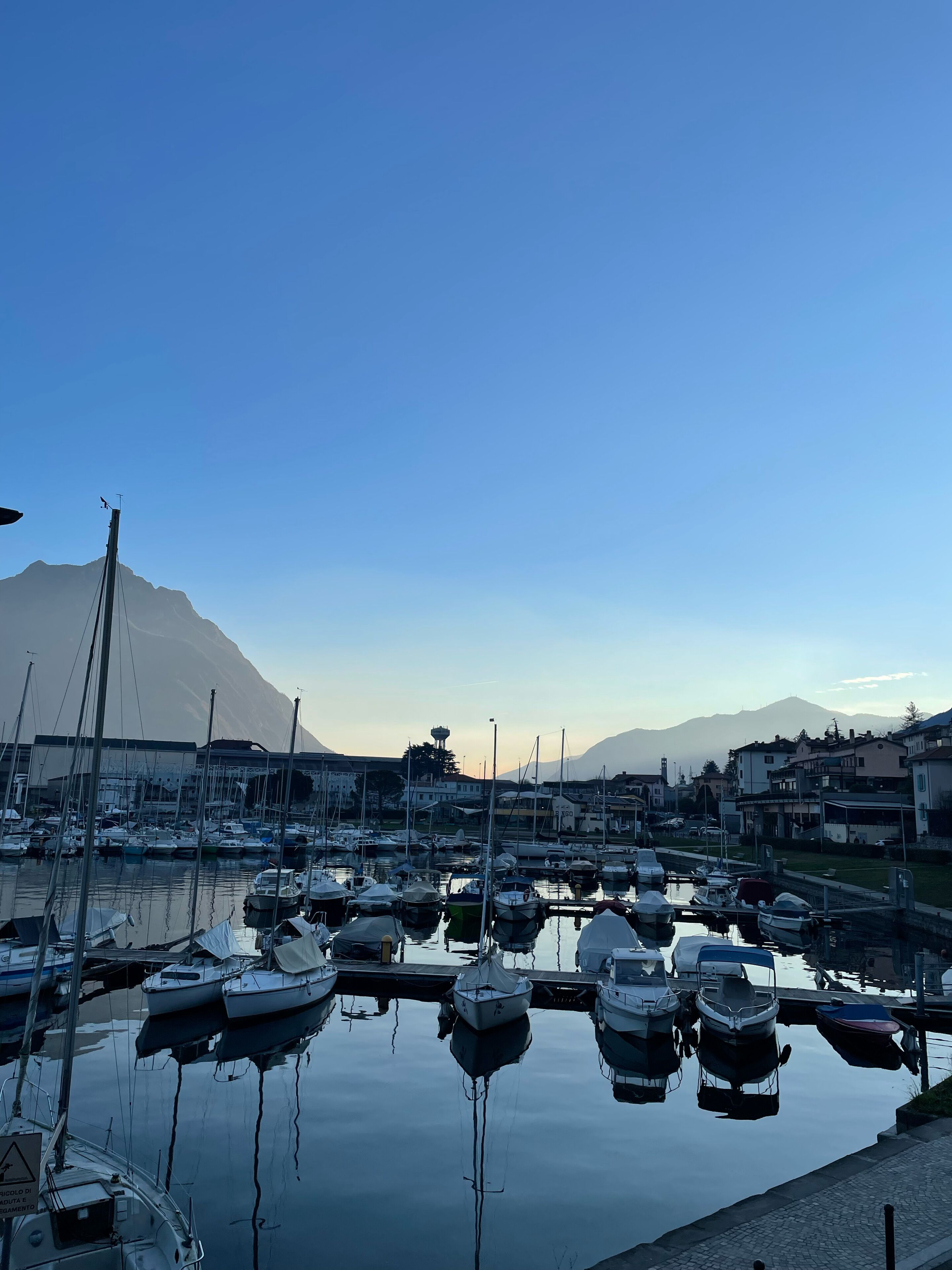 A marina with boats docked, a mountain in the background, and buildings along the waterfront.