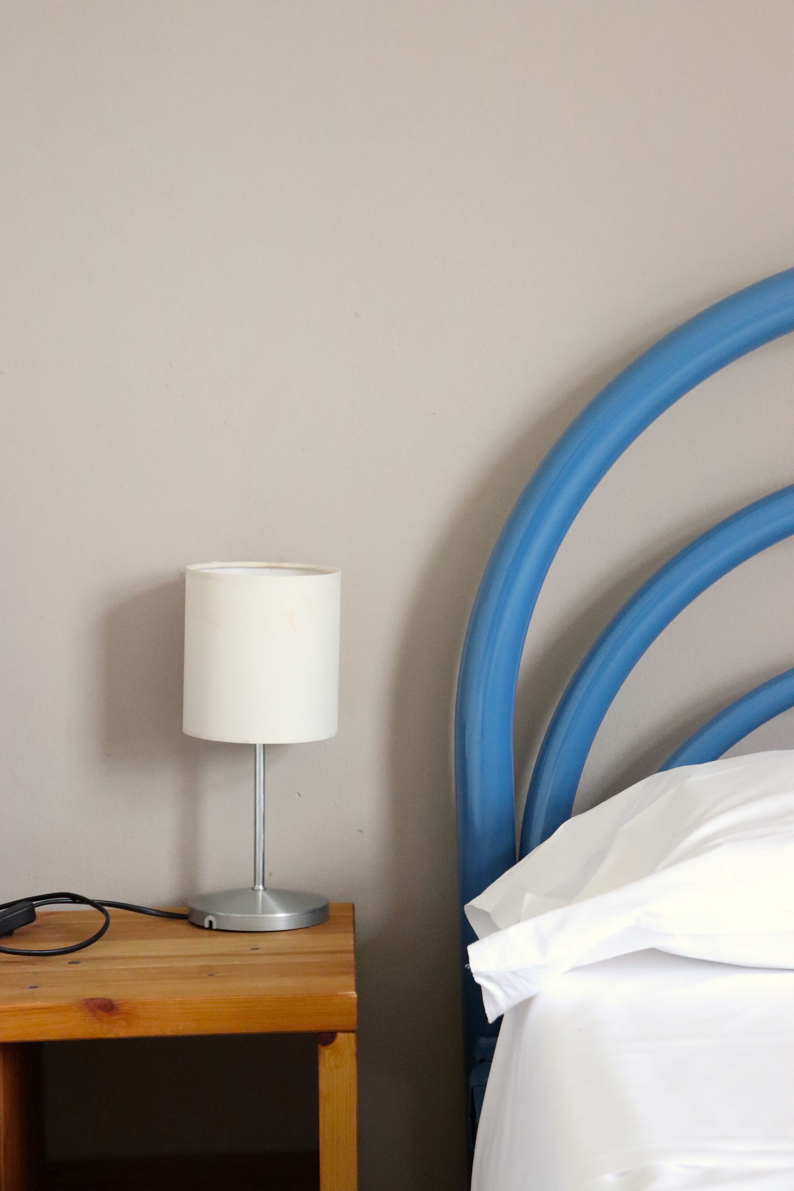 A bed with a blue headboard, a bedside table with a lamp, and a white pillow.
