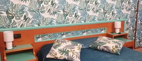 Un dormitorio con una cama, dos mesitas de noche, un cabecero de madera y una pared con un diseño de hojas.